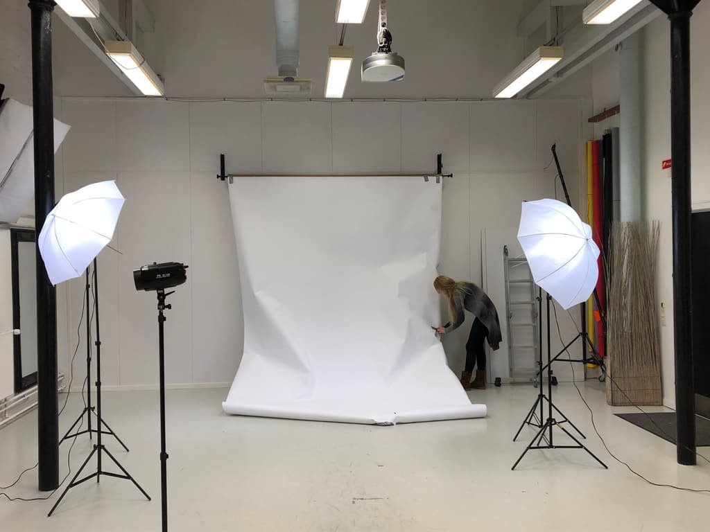 Bright studio with umbrella lights and a white paper backdrop